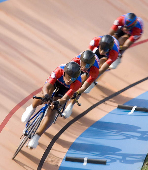 Image of four velodrome racers in a paceline going through a turn on a wood velodrome